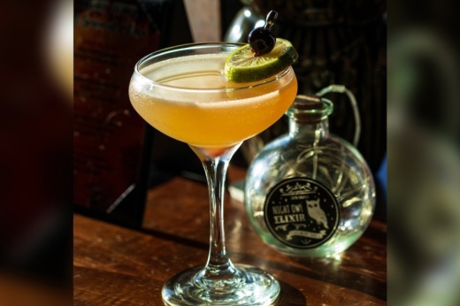 cocktail glass with an orange drink garnished with lime and a cherry