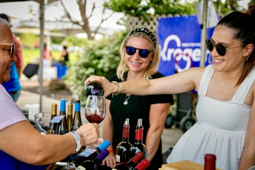 Two women pouring another woman a glass of red wine, all three are smiling