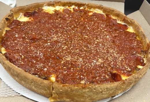 A photo of a deep dish pizza on a to-go cardboard box.