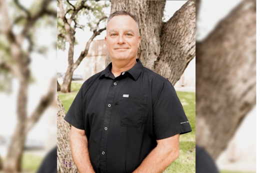 Liberty Hill ISD Chief of Police Chris Rybarski stands smiling in a black shirt in front of a tree.
