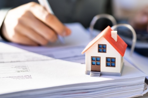 tiny toy house on a stack of papers someone is writing on