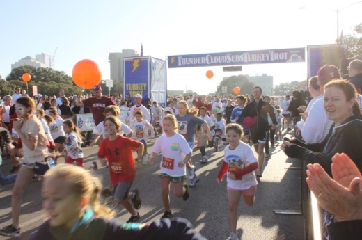 A group of people run from the start line outside on a sunny day at the Turkey Trot.