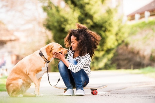 Girl sitting on skateboard pets golden retriever