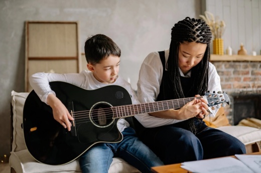 a woman placing a boy's fingers on the right fret on a guitar