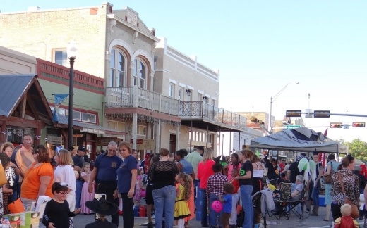 A big group of people, some in costumes, gather on Main Street in downtown Bastrop for a previous Halloween event.