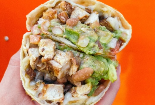 A hand holds a giant burrito stuffed with chicken and other ingredients.