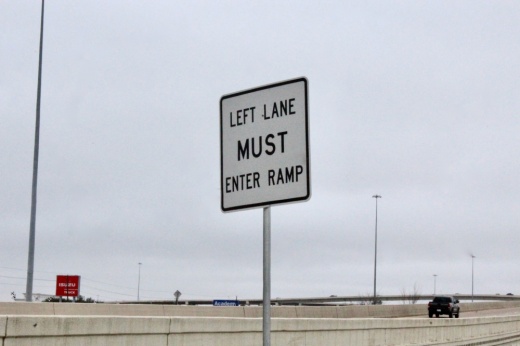 The photo shows a road and road sign that reads "Left lane must enter ramp."