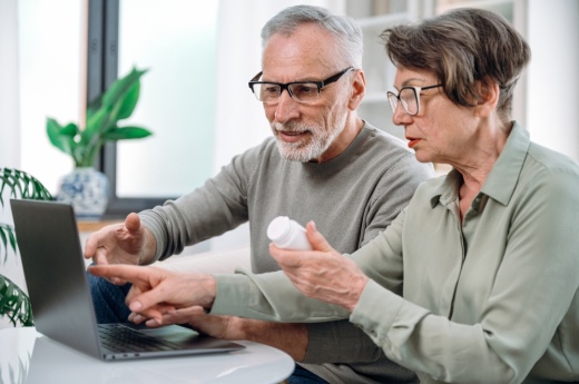 Senior couple using laptop, buying medication together online.
