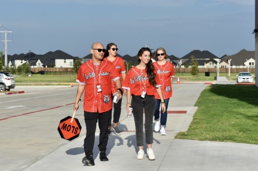 four middle school staff members in baseball shirts walk on the sidewalk next to a school