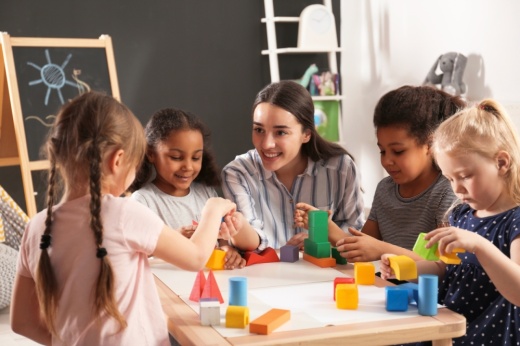 children and nursery teacher playing with building blocks in kindergarten