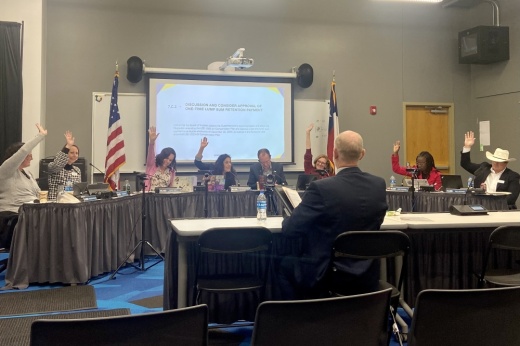 The Leander ISD board of trustees members raise their hands to take a vote.