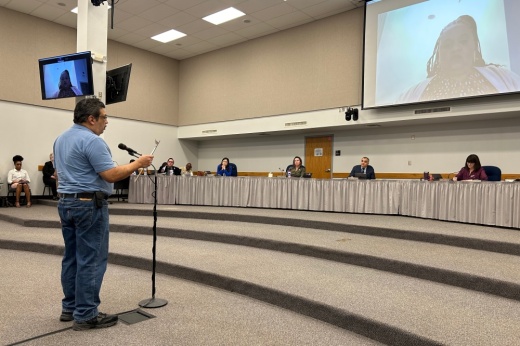 a person speaks at a microphone before the board of trustees