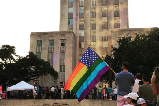 a man holds a pride flag while standing in front of Houston City Hall
