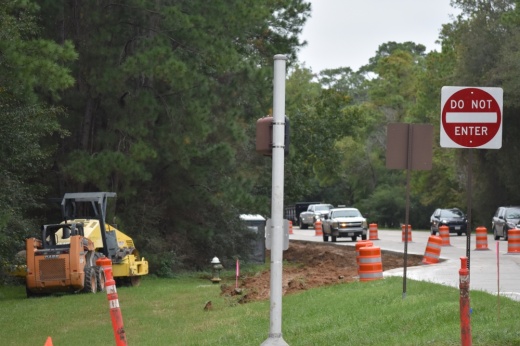 A construction vehicle is by the side of the road with orange barrels on the roadway.