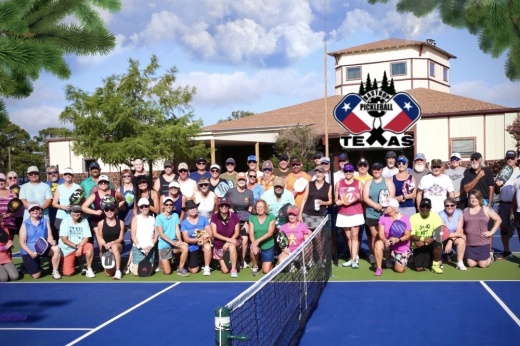 A group of adults posing for a photo at a pickleball court.