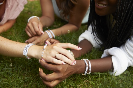 Three people wearing handmade bracelets by Little Words Project show off their jewelry to one another.