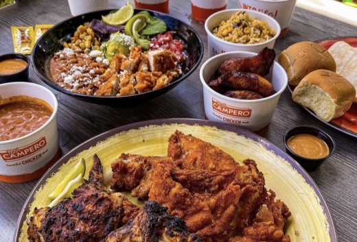 A table full of food, including a fried and grilled chicken plate, a chicken bowl, and sides.