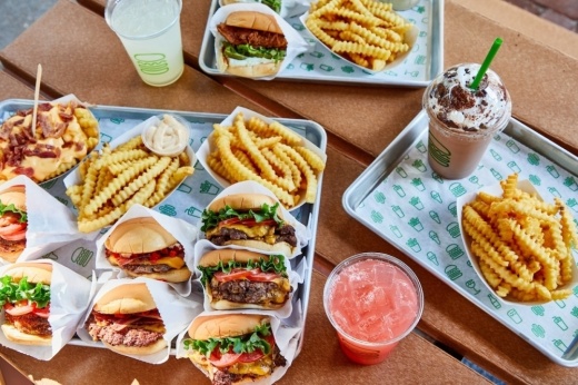 A table with trays holds a variety of burgers, fries and drinks.