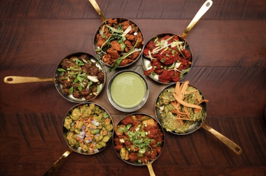 A table holds six dishes placed in a circle around a bowl of mint sauce.