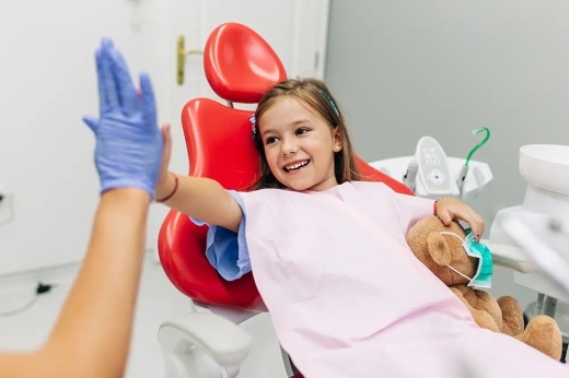 child in a dentist chair high-fiving someone with a medical glove on