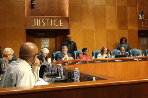 a group of people sit around a horseshoe-shaped desk in the houston city council chambers