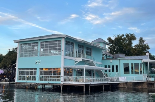 The exterior of Quince LakeHouse is shown with the lake underneath the aqua-colored building.