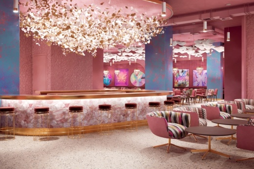 a large chandelier hangs over a pink dining area with a bar, tables and chairs
