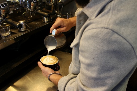 The photo shows a barista making a latte.