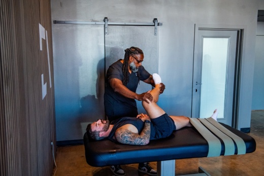 a man lies on a table while another man helps stretch his knee