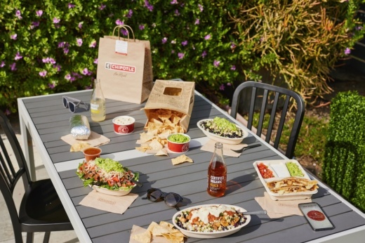 Chipotle meal consisting of Mexican bowls, chips and queso on a table outdoors.