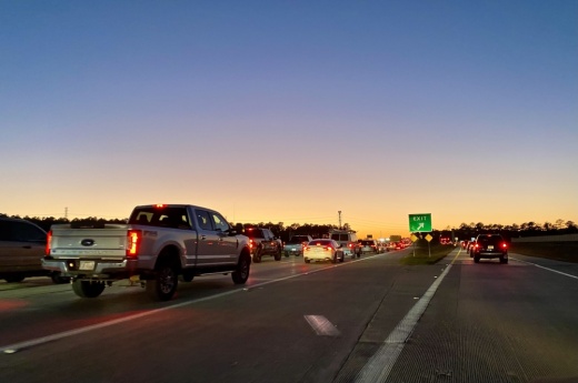 Cars and trucks travel down a highway at sunset.