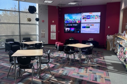 A room with three tables and chairs and a wall of four TVs