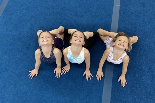 Three young girls do gymnastics on a blue mat