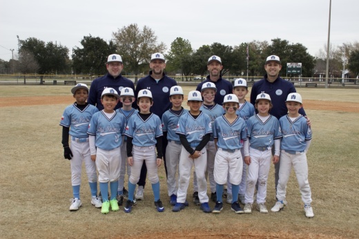 a group of children in baseball uniforms stand on a baseball field with four coahces behind them