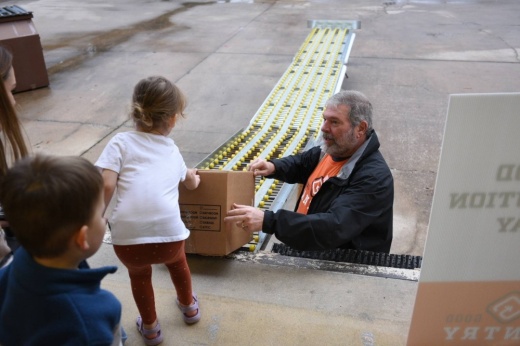 A volunteer at Local Good Pantry gives a box of food to a young girl.