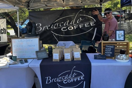 A person stands outside next to a vendor's booth filled with coffees for Brewcado Coffee.