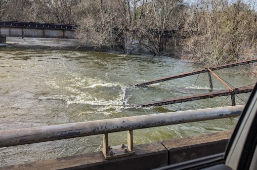 An iron truss bridge partially submerged in rushing waters.