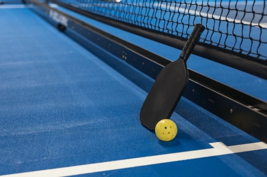 A pickleball paddle and ball against a net
