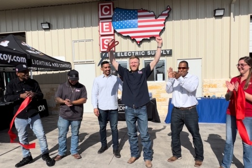 A group of people stand outside the new location in Bastrop while clapping after the ribbon cutting.