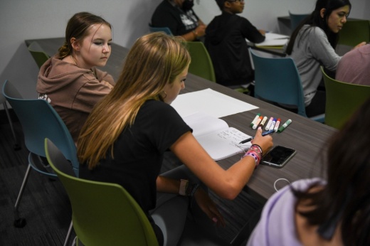 A student writes on a white piece of paper on a desk