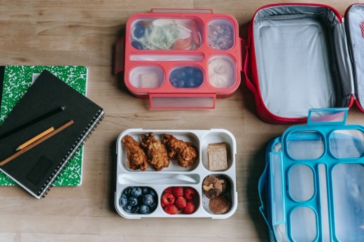 The photo shows two trays of food next to lunch boxes and notebooks.