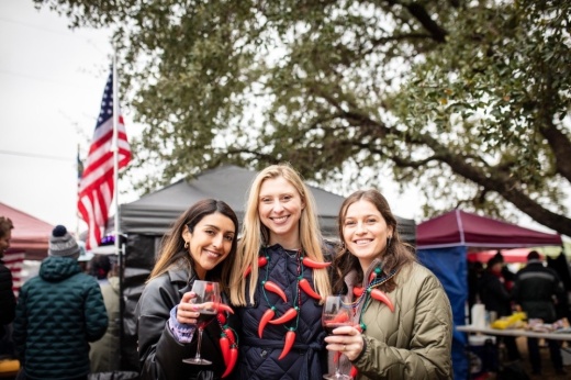 Three women standing in front of the camera smiling. Two of them on the left and right are holding wine glasses with red wine. All three have red pepper necklaces around their necks