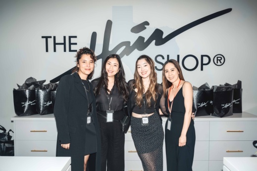 Four women stand next to each other in front of a wall with The Hair Shop logo painted on it