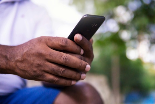 A man's hands are holding a mobile phone in the photo's foreground.