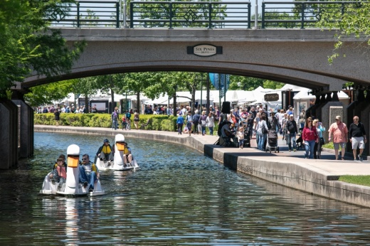 Swan boats travel under a bridge on the waterway with crowds in the background