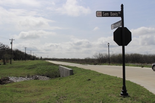 Picture of a stop sign and intersection and land in the background.