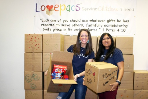 Two females holding boxes standing in front of boxes with a Lovepacs banner in the background.