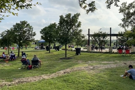 A large grass area with people watching a stage.