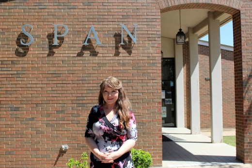 Woman standing in front of a brown brick building with SPAN signage.