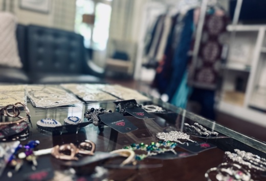 A table is shown in the foreground with jewelry spread out, and a clothing rack in the background.